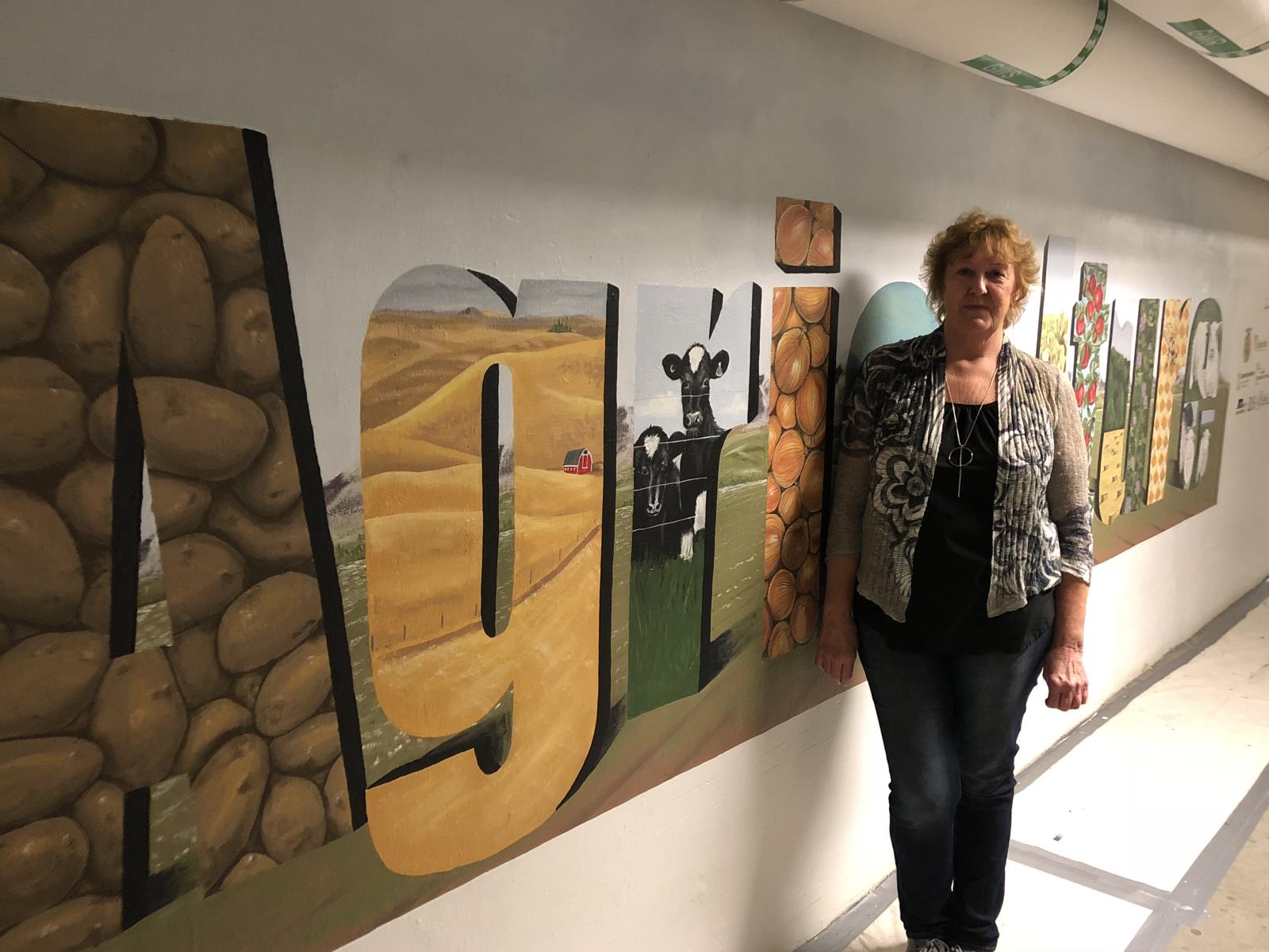 Parma High School art teacher Linda McMillin stands next to a large agricultural-themed mural she painted in underground tunnel beneath Idaho’s Capitol building. 